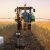 Sunrise in a wheat field with an autonomous tractor and a farmer holding a smartphone while using climate-smart soil monitoring.