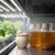 Indoor hydroponic grow room with fresh green herbs in channels, alongside glass jars and a ceramic crock suggesting fermented natural farming inputs.