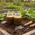 “Dark, crumbly organic soil in a garden bed with leafy plants and homemade microbial preparation jars with natural liquid beside simple tools.”